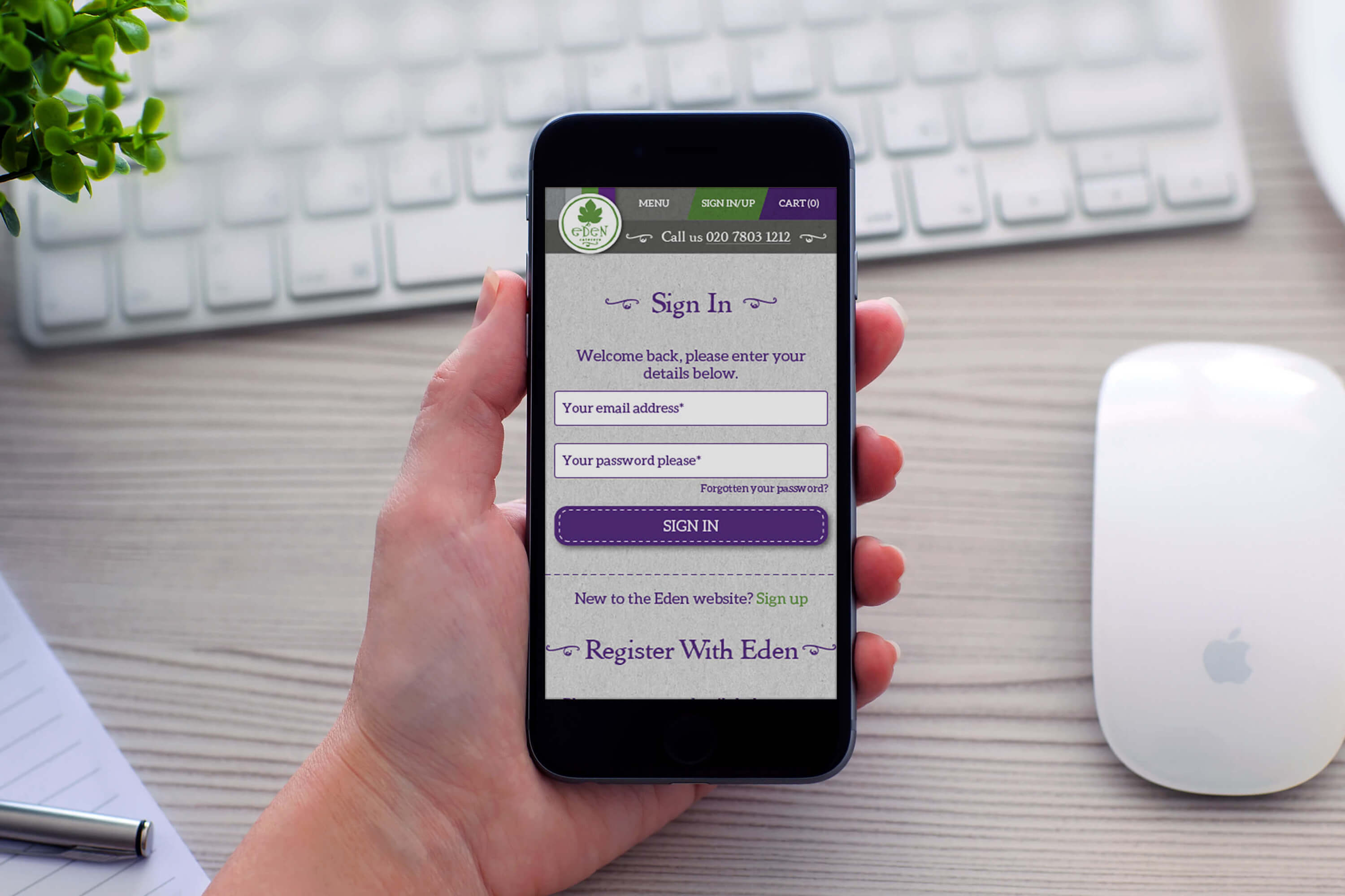 A woman at a desk holding an iPhone showing the account login page design for the Eden Caterers website