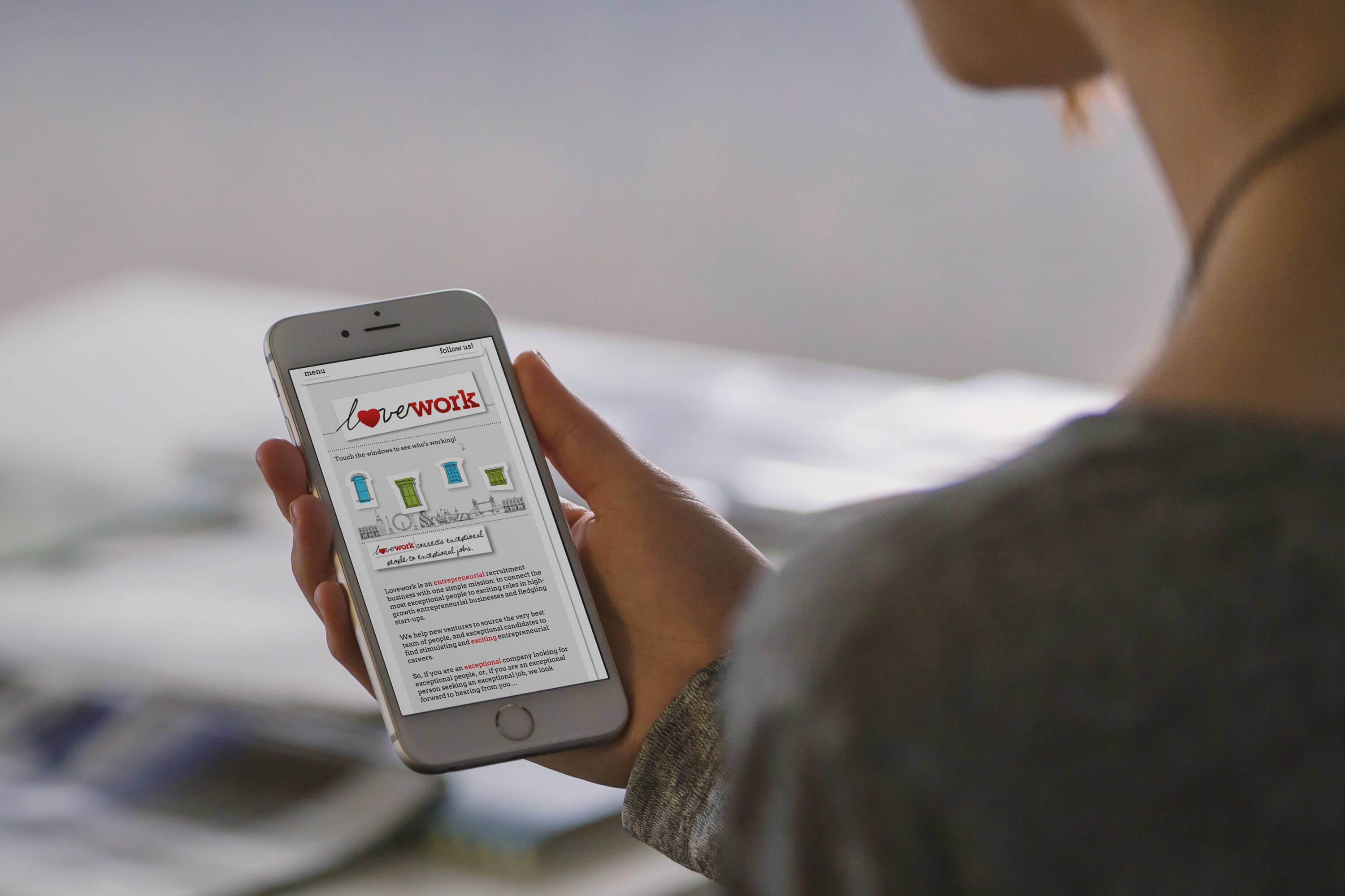 A woman holding an iPhone displaying the Lovework website home page design